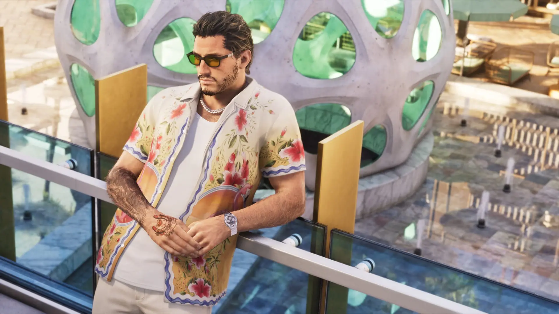 Man in sunglasses and a floral print shirt leans on a glass railing beside a round white building with green windows.