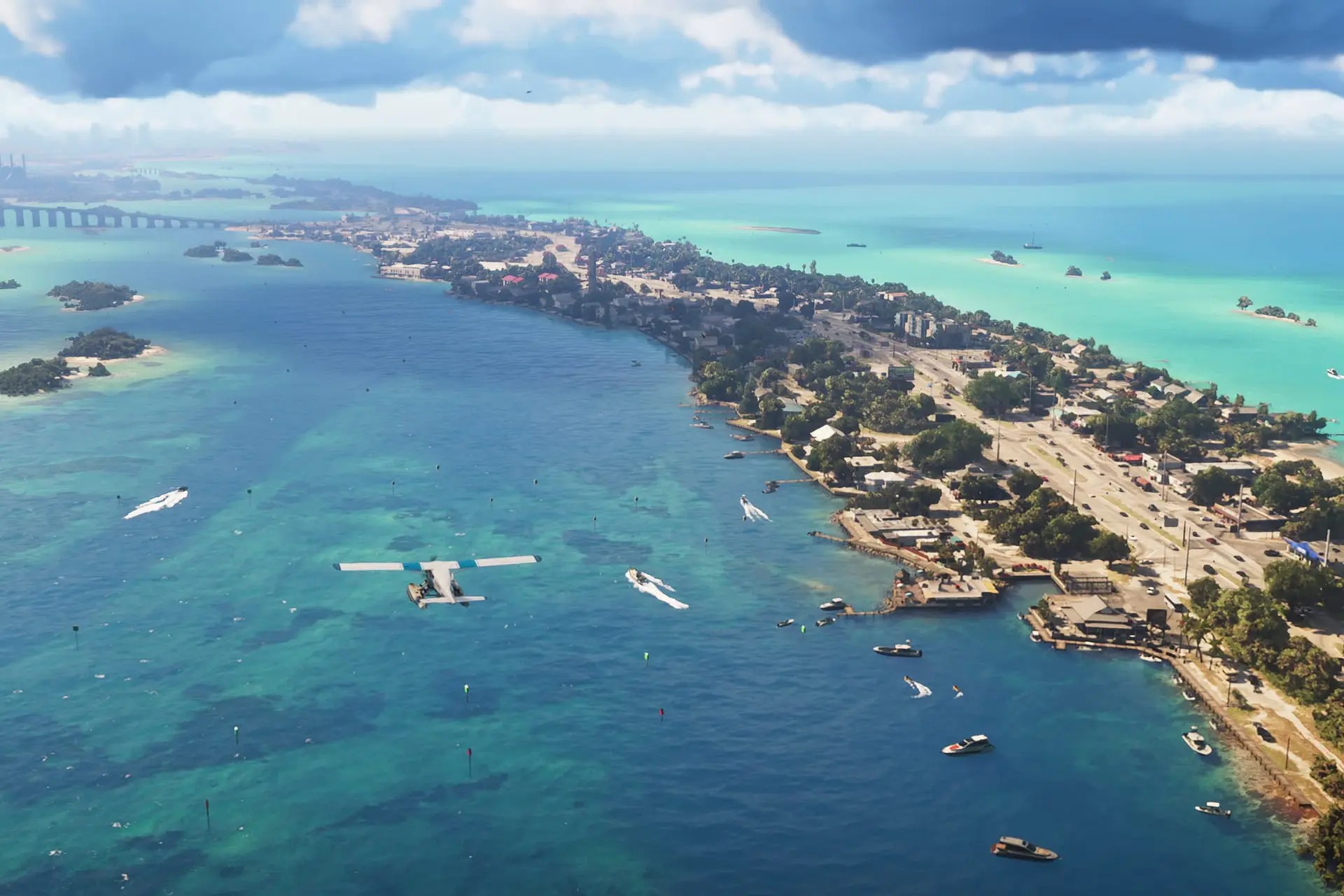 Aerial view of a coastal town with a seaplane floating on turquoise water, boats scattered nearby and a long bridge in the distance.