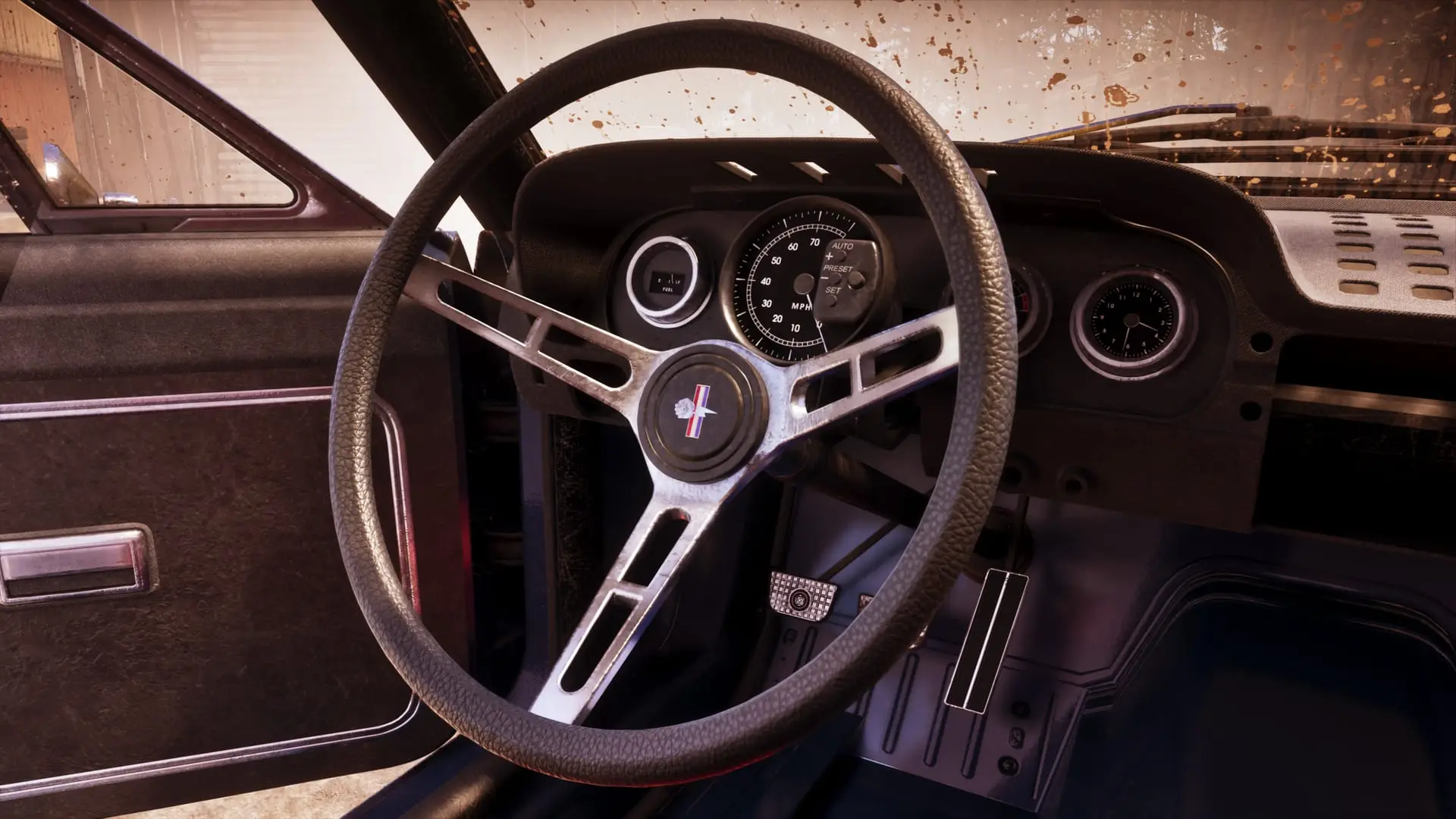 Steering wheel and dashboard of a vintage car, seen through a rain-speckled windshield.