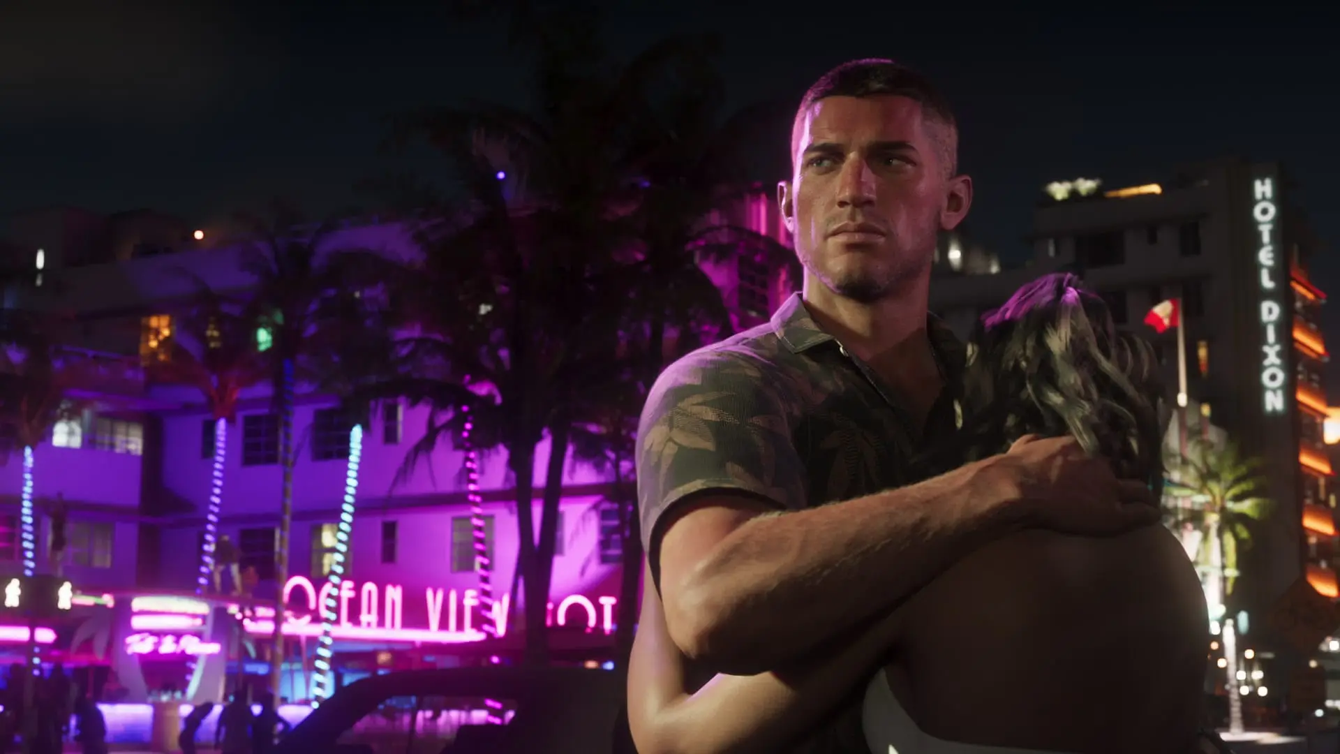 Man in a camo shirt holds a woman at night beside a neon-lit purple building, palm trees and a Hotel Dixon sign behind them.