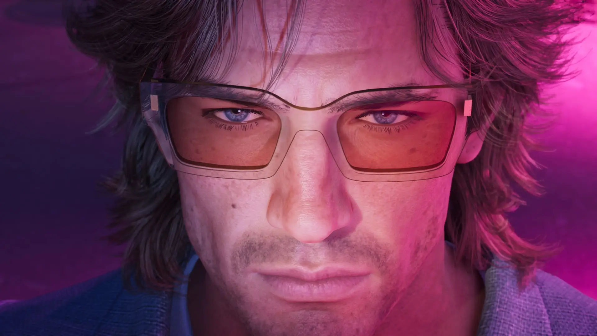 Close-up of a man with orange-tinted glasses and stubble, lit in pink and purple light.